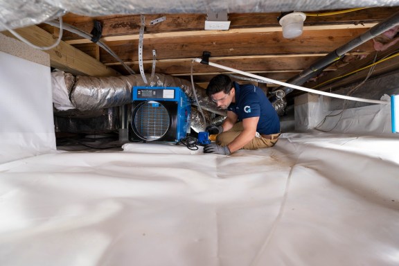 A worker installing a dehumidifier in a crawl space.