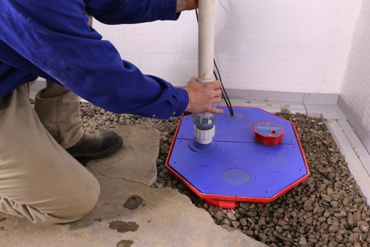 Production crew installing sump pump in basement