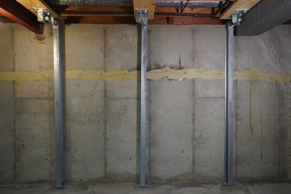 Basement wall with steel support beams and a visible horizontal crack repaired with sealant.