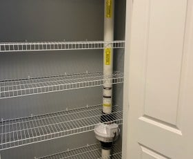 Empty wire shelves in a closet with a radon mitigation system installed on one side.