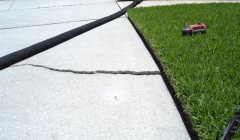 Cracked concrete on sidewalk of home next to grassy yard