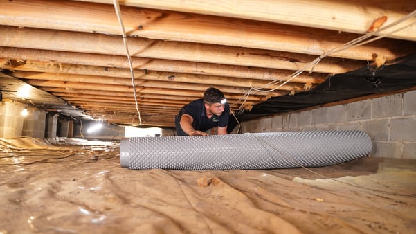 A Groundworks worker installing drainage matting in a crawl space.