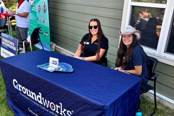 Two people sitting at a "Groundworks" table outdoors, with informational materials displayed.