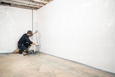 a man extending sump pump discharge pipe line in corner of basement