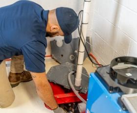 service tech working on a sump pump in the basement and explaining how a sump pump can help when it floods in the area