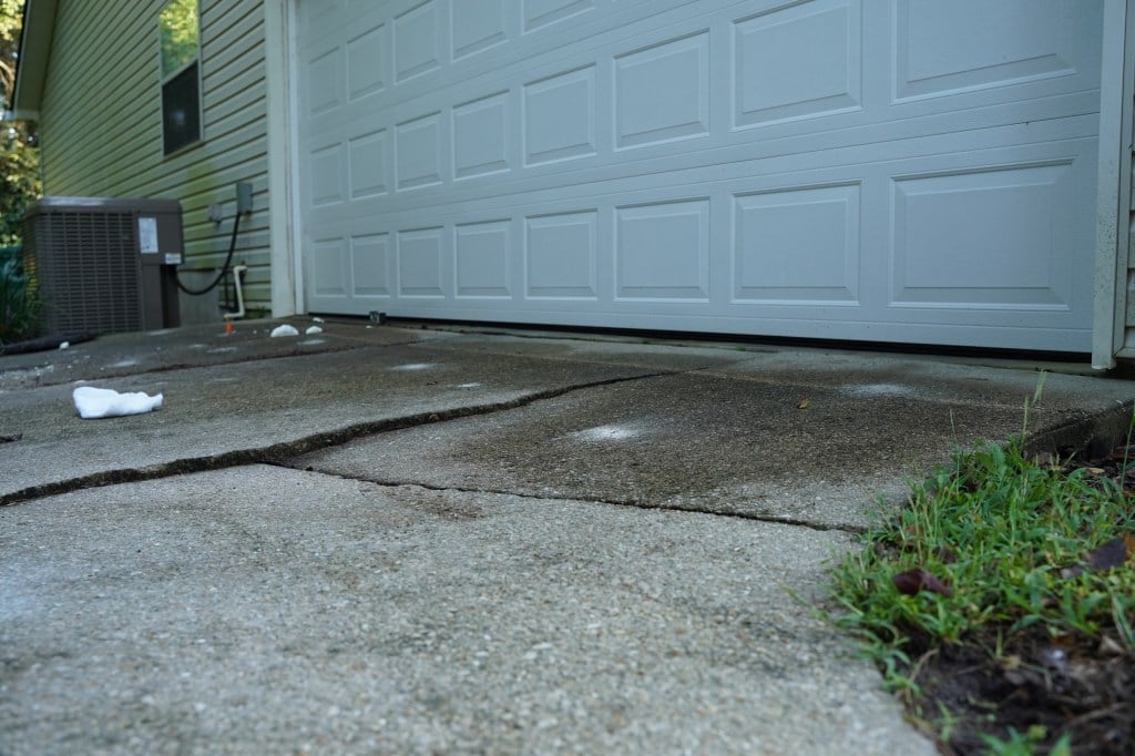 Sunken concrete driveway in front of a closed garage door, with grass on the side and an air conditioning unit.