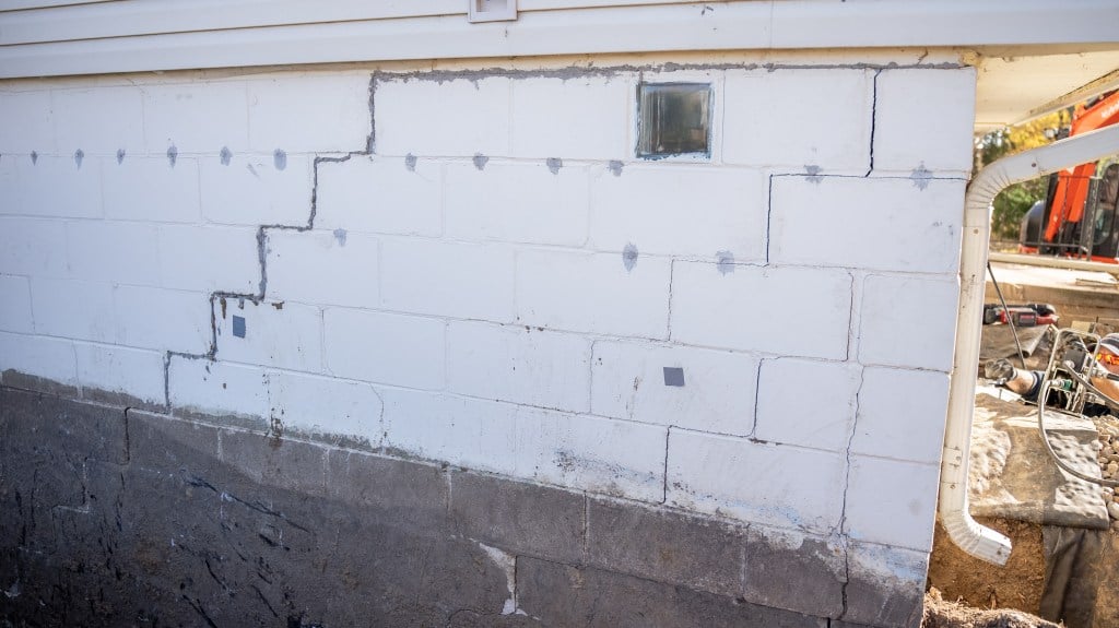 Cracked white foundation wall with visible repair work and a small glass block window.